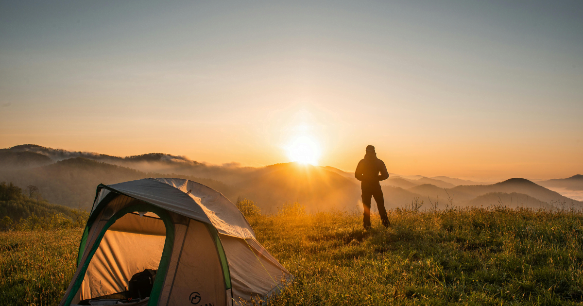 A man looking at a sunset next to a tent